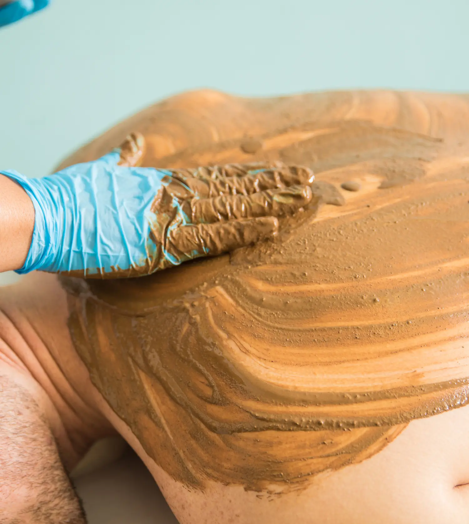 Therapist applying a mineral-rich mud application to a client's back during their Ultimate Back Treatment spa experience at Pause Spa